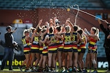 The whole Adelaide Crows team stand in a huddle and celebrate, squirting water everywhere
