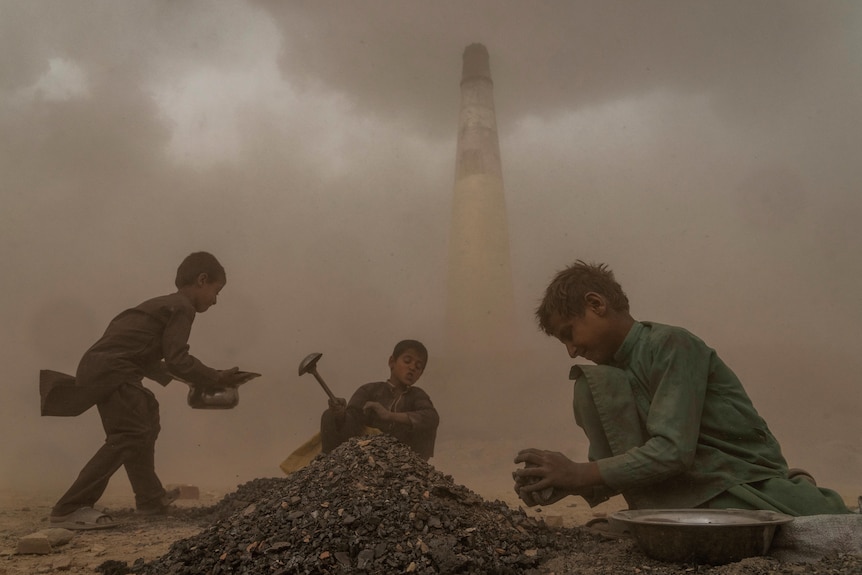 three children work near a pile in a dusty brick factory in afghanistan