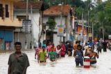 People walk along a flooded road in waist deep water.