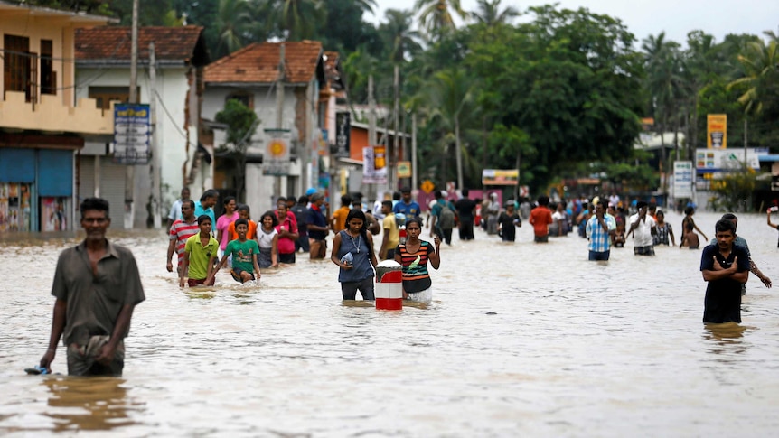 People walk along a flooded road in waist deep water.