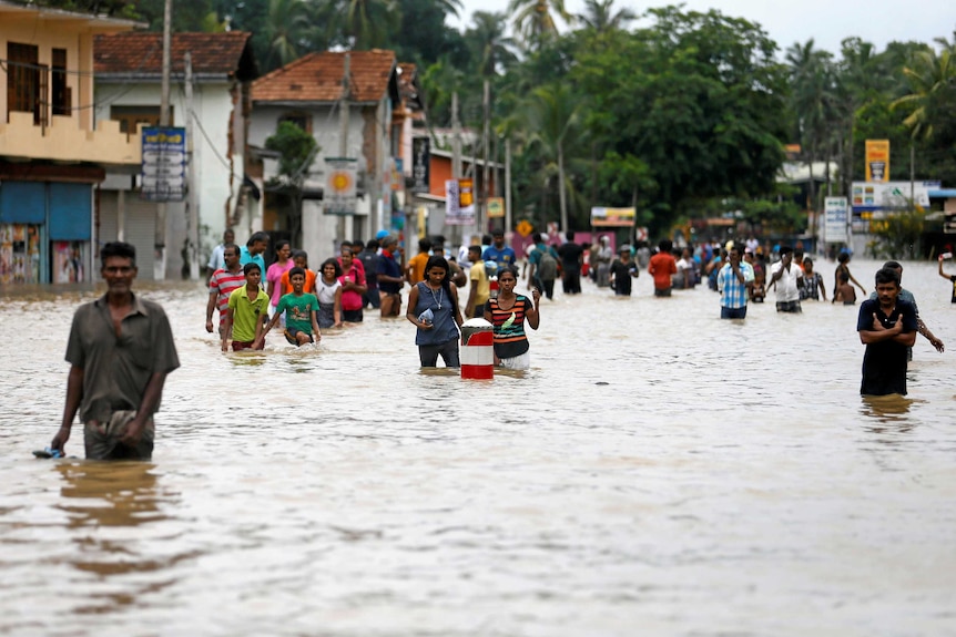 People walk along a flooded road in waist deep water.