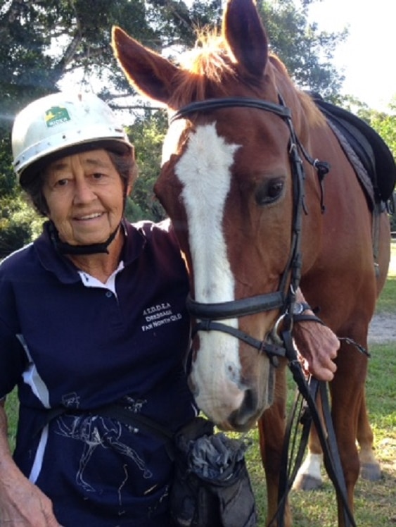 Esther Brooks in her riding helmet, standing next to her chestnut coloured horse, with their heads side by side