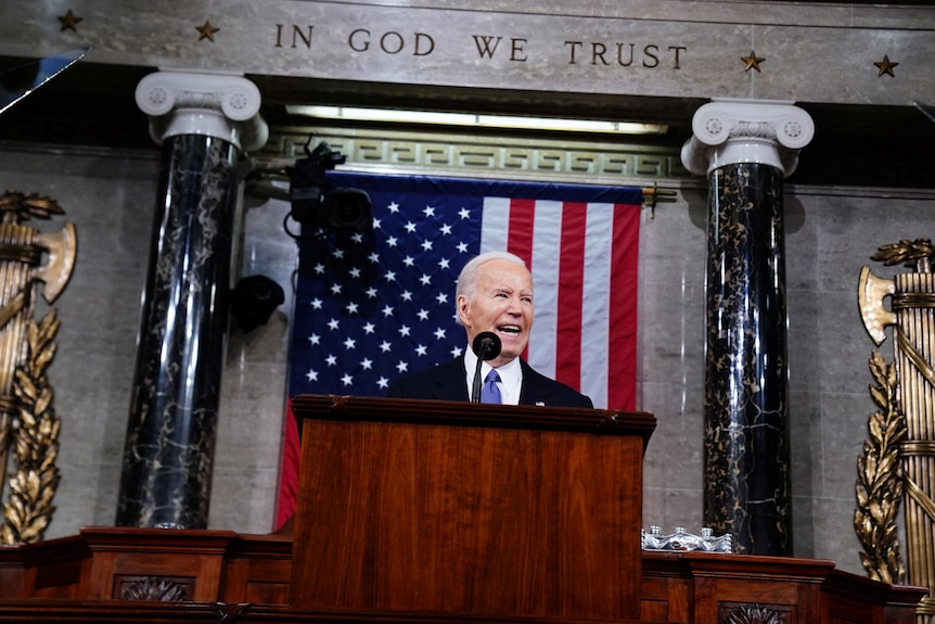 Joe Biden stands at a podium in front of a United States flag.