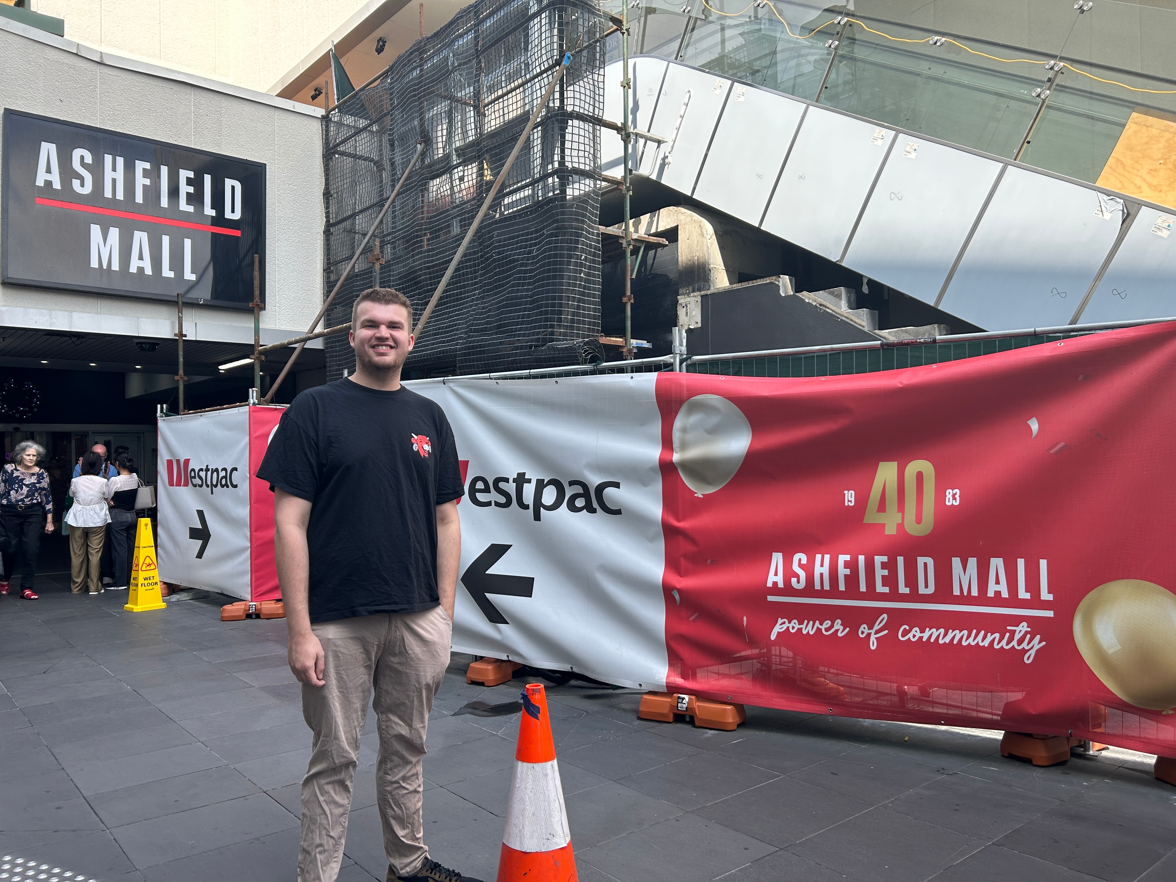 A young man stands at the mall entrance with escalators wrapped in scaffolding. 