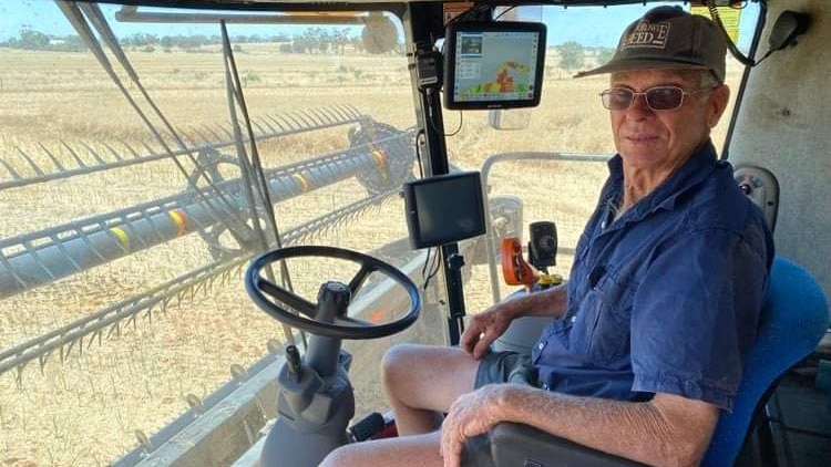 Ken Walter wears blue shirt and shorts. Behind the wheel of a harvester.