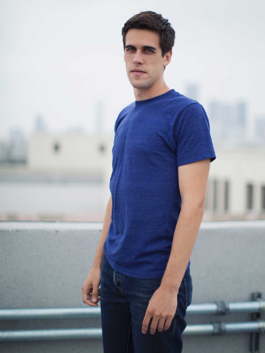 Ryan Holiday stands on a rooftop with a city in the background.