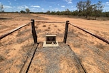 A fenced off grave marker surrounded by red sand and bushland.