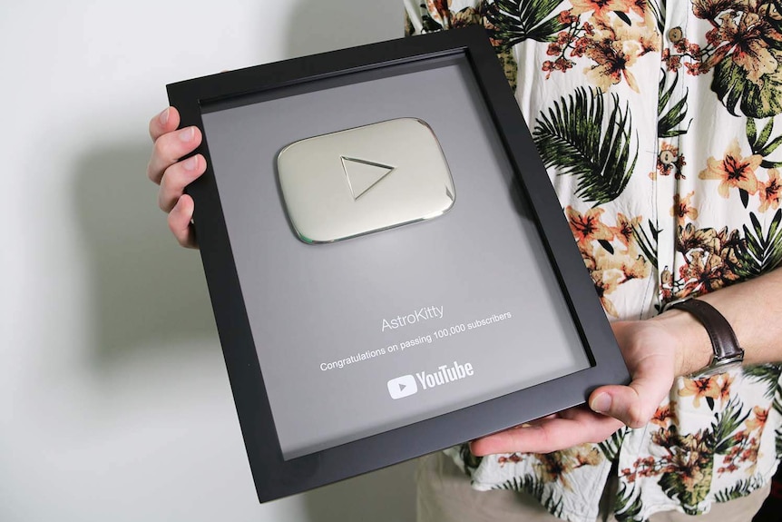 Alex Hockings holds a plaque from YouTube congratulating on him surpassing 100,000 subscribers.