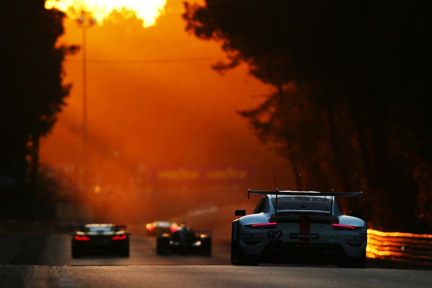 One hyper race car in the the foreground, driving away from shot, into a sunset with other cars ahead.
