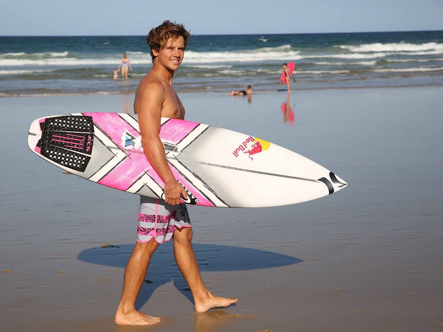 Surfer holding a surf board with hot pink design at the beach