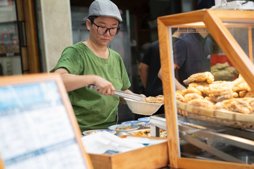 A Taiwanese chef tongs food into bowls at the street food stall she runs