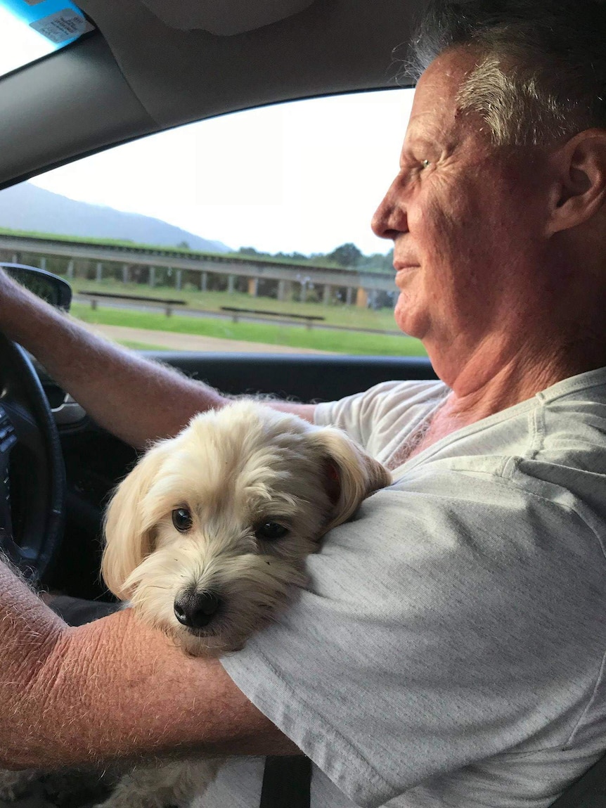A man driving while holding a small white dog.