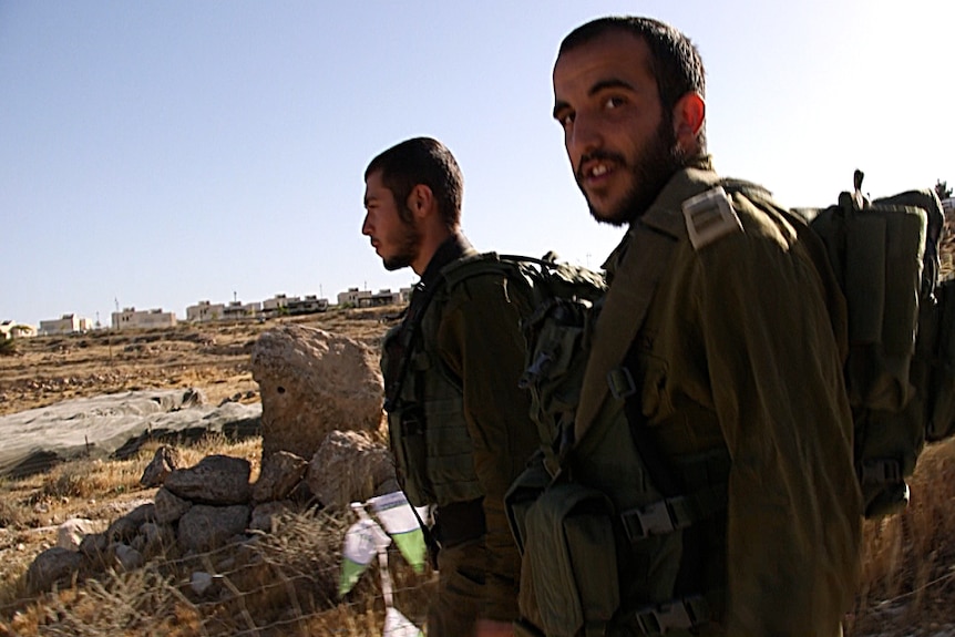 Two Israeli Defence Force troops walk, accompanying teenagers on their way to school, past an Israeli settlement.