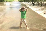A young girl wearing a green shirt playing in shallow flood water.