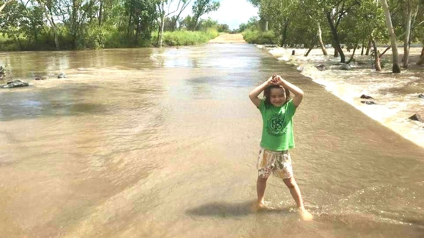 A young girl wearing a green shirt playing in shallow flood water.