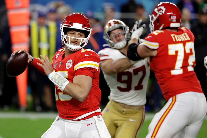 Patrick Mahomes looks up and prepares to throw the ball. A blocker stops a tackler in the background.
