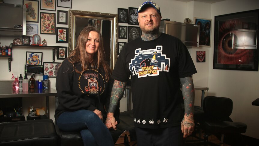 Lance Daly holds the hand of his wife Rebecca inside their tattoo shop.