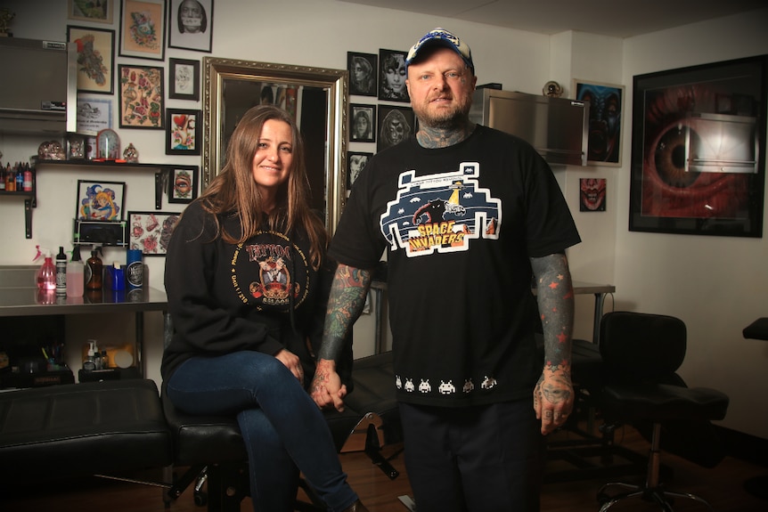 Lance Daly holds the hand of his wife Rebecca inside their tattoo shop.