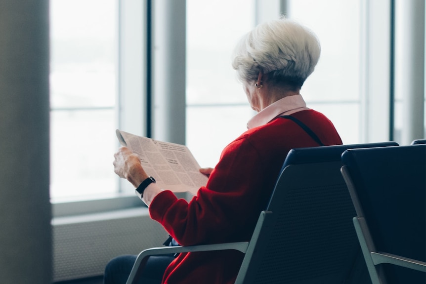 A woman with grey hair reads a newspaper on her own