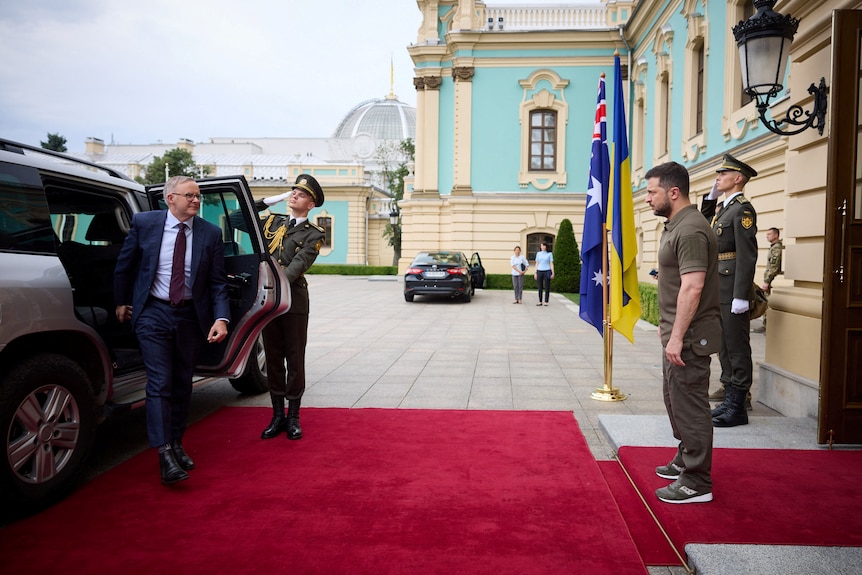 Albanese steps out of a car onto a red carpet, as Zelenskyy stands waiting to greet him.