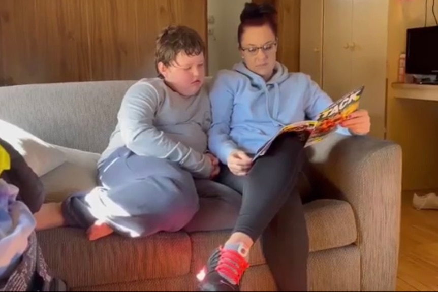 A mother and her pre-teen son sitting on a couch reading a book together.