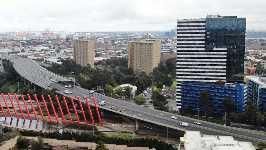 On an overcast day, you view a new residential tower behind a raised freeway, with older public housing towers adjacent to it.