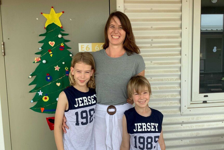 Bronwen Seal and her sons Elliott and Toby smile at the camera. On their quarantine donga door is a Christmas tree.