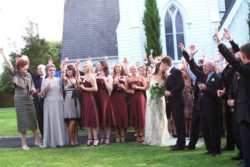 A group of people celebrating a newly-married couple as they kiss.