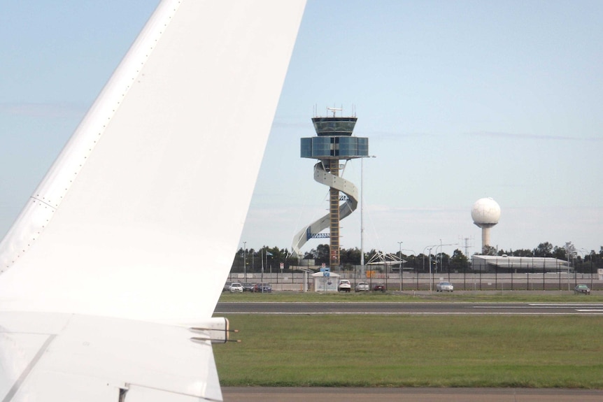 Photo from plane window of one of the wingtips with the control tower and a radar in the distance.