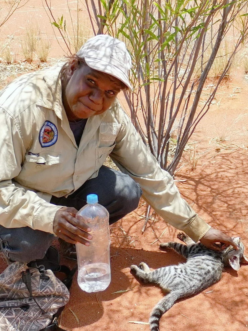 Indigenous ranger with a feral kitten on red dirt