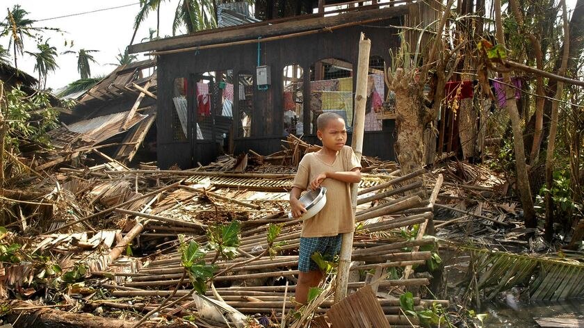 A boy stands next to the remains of his family's house