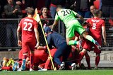 Adelaide United players jump into a pile of bodies in front of spectators in a grandstand