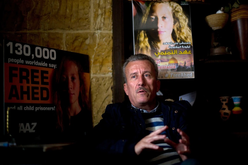 A man sits and talks in front of several posters.