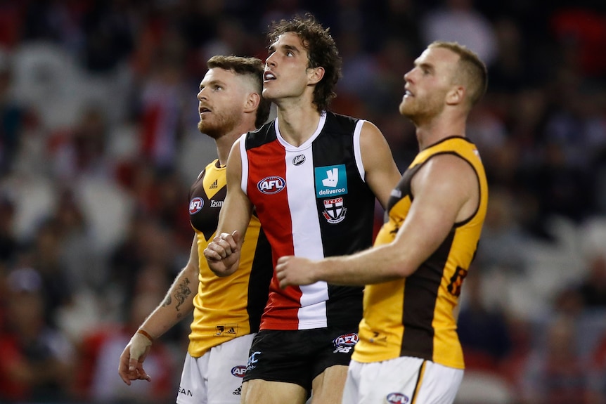 One St Kilda player and two Hawthorn players watch the ball sail away during their AFL game.