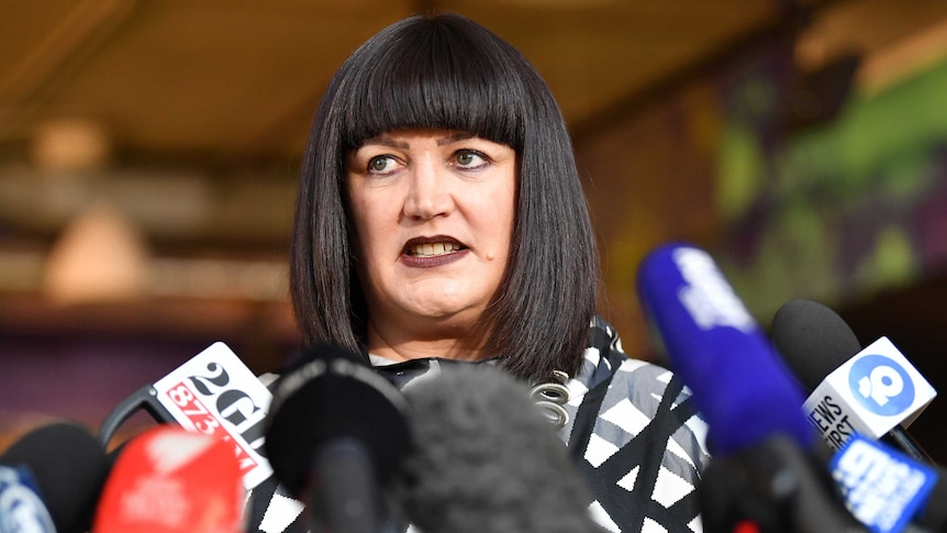 A woman stands in front of a bank of microphones at a press conference.