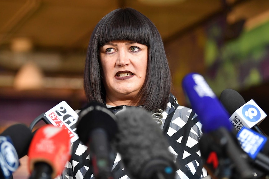 A woman stands in front of a bank of microphones at a press conference.