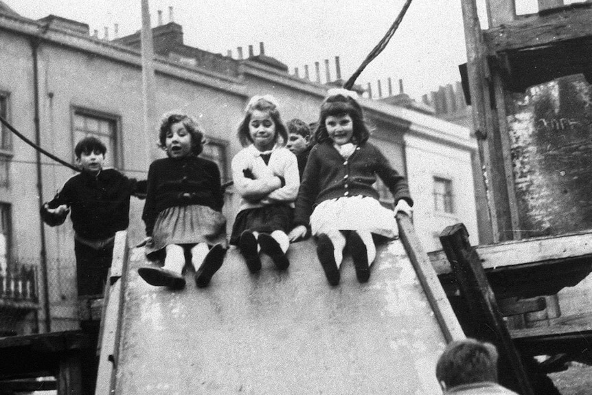 A black and white photo of children in the 60s playing on playground equipment, the image is dominated by three little girls.