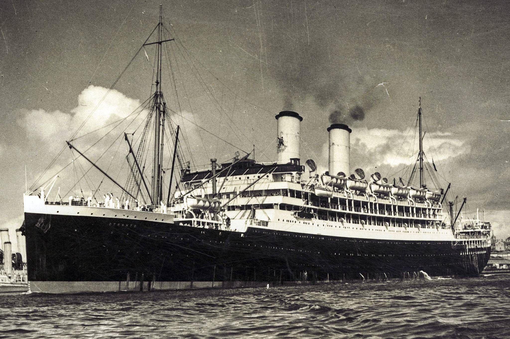 A black and white photo of a large ocean liner departing port 