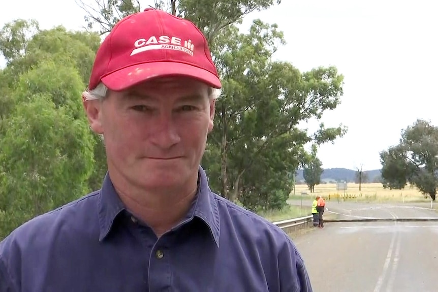 A man in a red cap stands in front of a collapsed bridge.