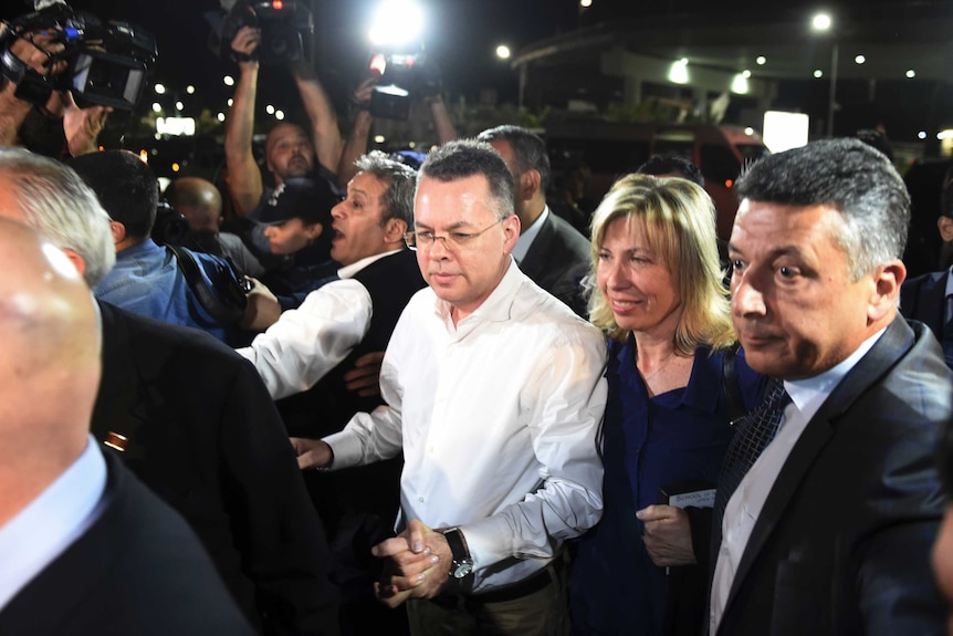 Pastor Andrew Brunson grasps the hand of his wife as they arrive at an airport surrounded by press.