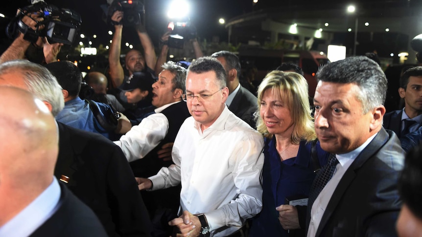 Pastor Andrew Brunson grasps the hand of his wife as they arrive at an airport surrounded by press.