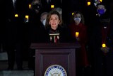 Nancy Pelosi speaks at a podium in front of members lining the Capitol steps and holding candles
