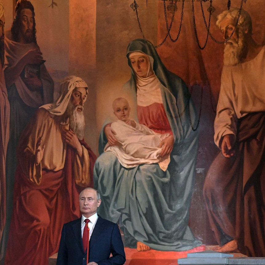 vladimir putin in suit holds candle in front of enormous russian orthodox painting of mary holding divine baby jesus and 4 men