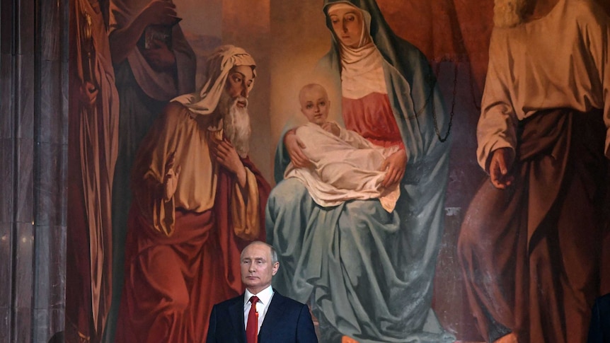 vladimir putin in suit holds candle in front of enormous russian orthodox painting of mary holding divine baby jesus and 4 men