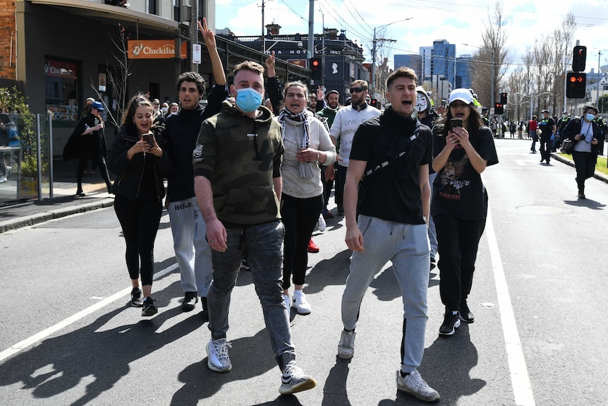 Anti-lockdown protesters, many not wearing masks, stand and yell outside the Queen Victoria Market.