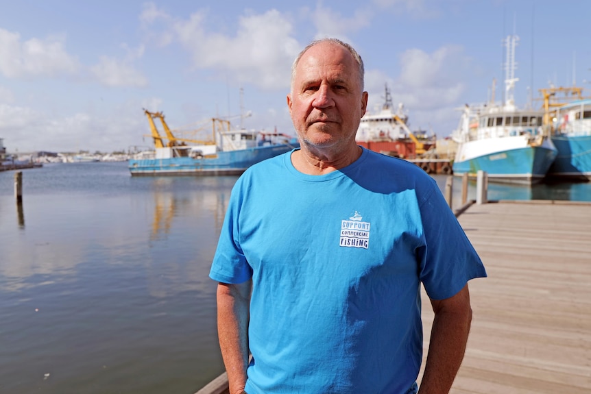 A serious man in a blue shirt at a boat harbour.