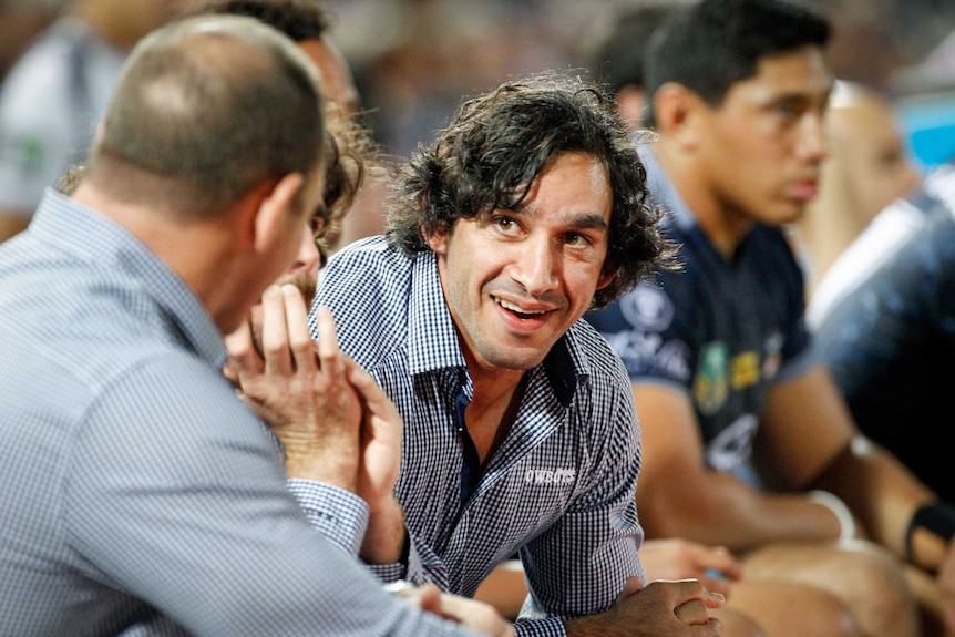 North Queensland Cowboys co-captain Jonathan Thurston chats with someone on the sidelines, wearing a blue and white checked shi