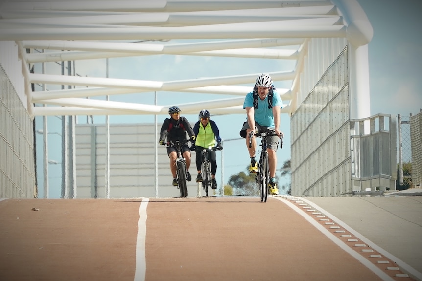 Three cyclists pedal over a bridge
