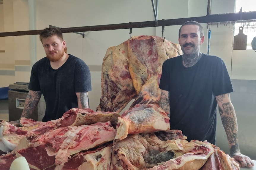 Two butchers stand behind a giant pile of pork.