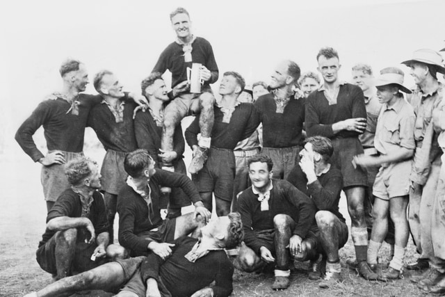 Black and white photo of man holding trophy sitting on teammates shoulders